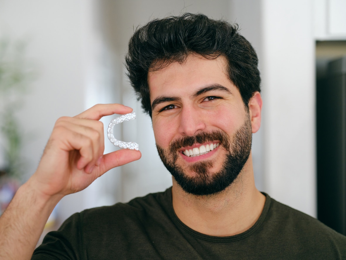 Adult patient smiling and holding his Invisalign clear aligner