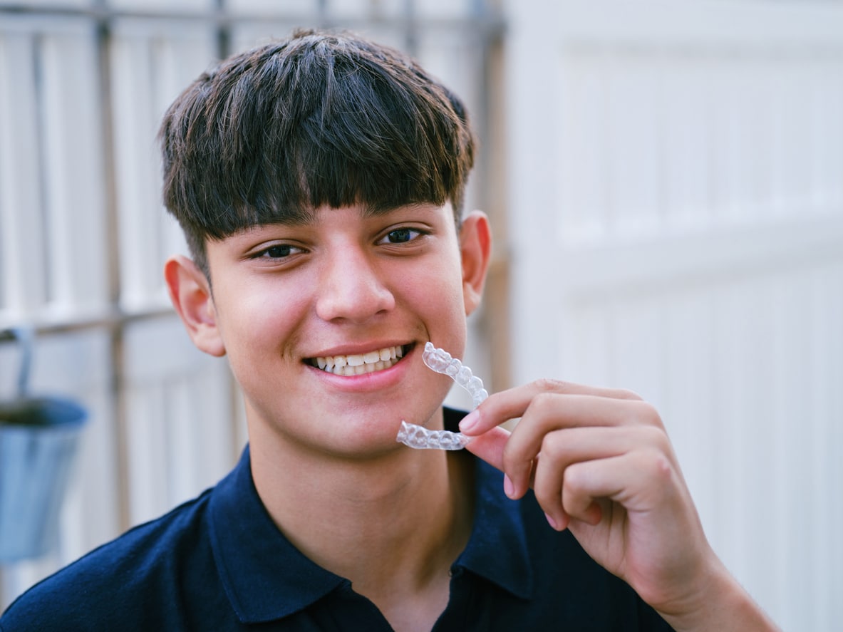 Teen patient smiling and holding his Invisalign clear aligners in Phoenix