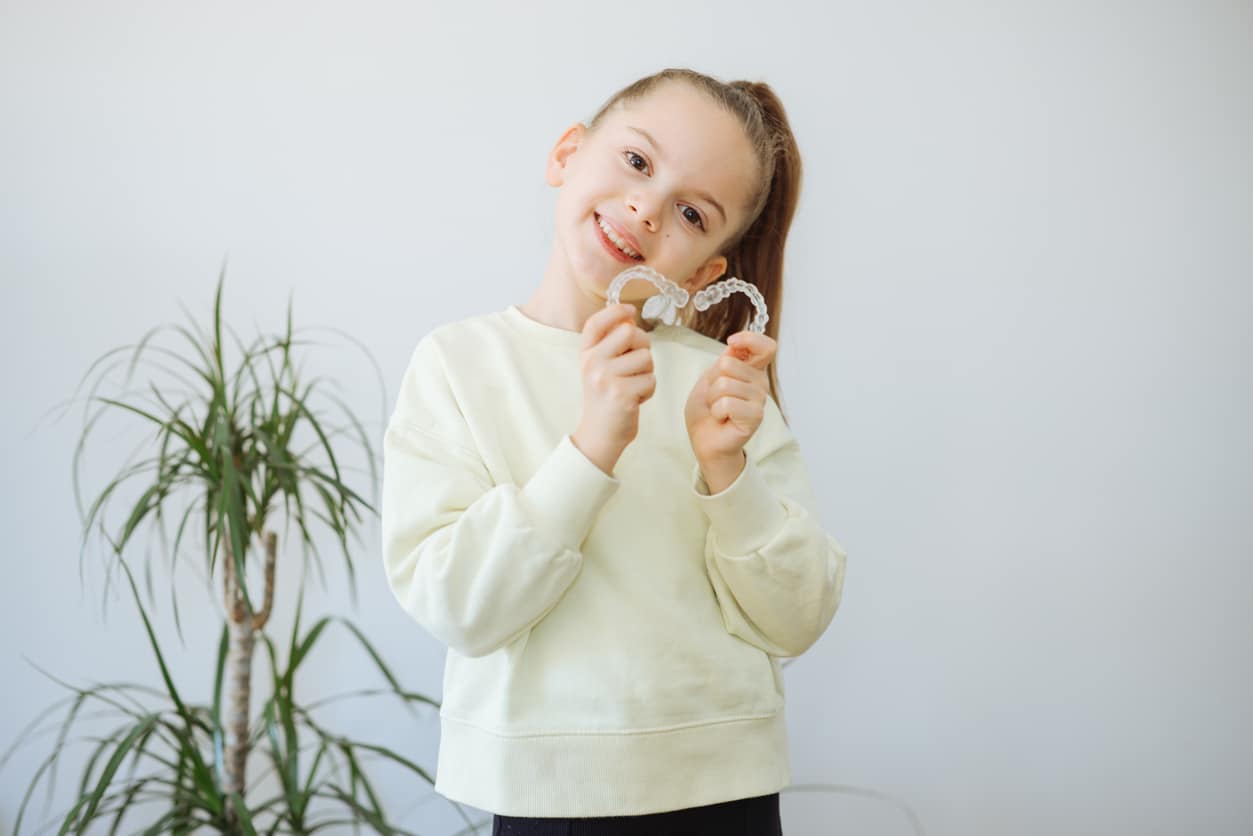 Young patient smiling and holding her Invisalign clear aligners